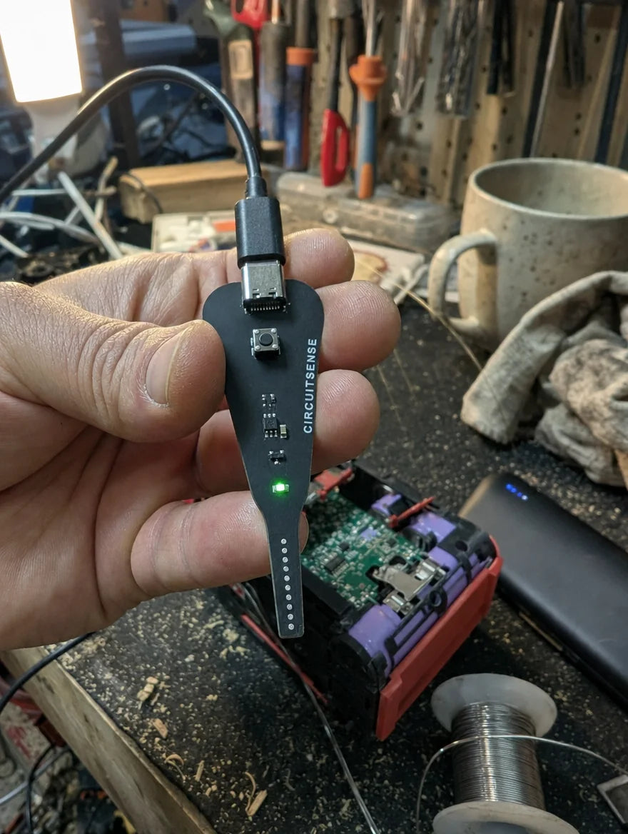 Photo client : sonde CircuitSense tenue devant une batterie de visseuse ouverte sur un établi de garage