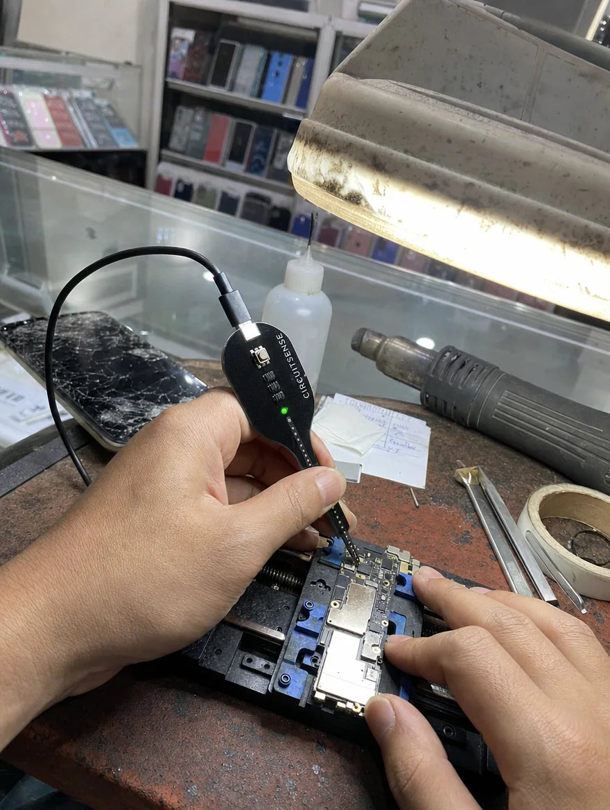 Photo client : sonde CircuitSense sur une carte mère de smartphone au comptoir d'une boutique de réparation