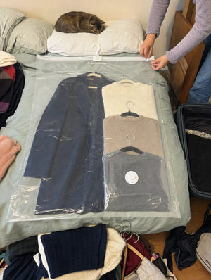 Photo cliente : housse SupremeStorage posée sur le lit avec un manteau et trois pulls, fermeture du zip